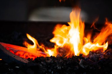 Parlak alevler ve kömürle demirci ocağında yanan sıcak metal.