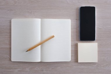 Akıllı telefonun yanına kalem ve ahşap masanın üzerine yapışkan notlarla birlikte defteri aç