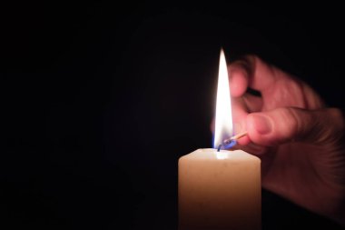 Tamamen karanlık bir odada bir kadının eli kibritle mum yakıyor. Elektriksiz yaşam kavramı.