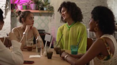 4k Genç Igbt insanları konuşuyor ve eğleniyor, kafede masaya oturuyorlar. Güzel lezbiyen kadınlar, erkek gülücüklerle konuşuyor ve bakıyor, masasında içeceklerle oturuyor. Neşeli homoseksüel arkadaşlar