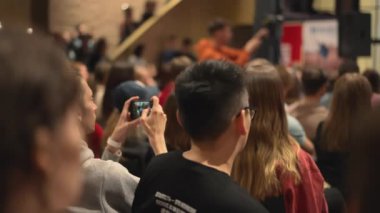 Etkinlikte, bir adam sanat ve eğlenceyi paylaşan kalabalığın fotoğrafını çekerek heyecanı yakalıyor. Oda eğlenceli bir seyirciyle dolu.