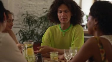 4k genç lgbt insanları barda masada konuşur ve içecek içerler. Gülümseyen, konuşan, alkol içen ve iç mekanda masa başında oturan çok ırklı güzel arkadaşlar. Çekici kadınlar, dostum.