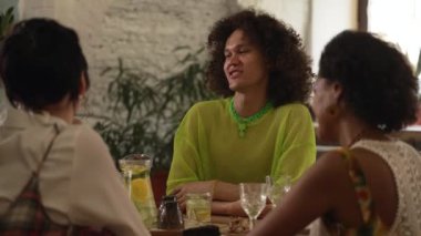 4k Yetişkin lgbt insanları modern bardaki masada içki içip sohbet ediyorlar. Çekici bir erkek, gülümseyen, gülen, kokteyl içen ve masasında oturan kadınlar. Mutlu