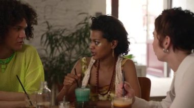 4k yakışıklı lgbt insanları kokteyl içer, konuşur, kafede masaya otururlar. Çekici genç kadınların portreleri, gülümseyen ve alkol içen bir adam, iç kısımda masa başında oturuyor. Grup