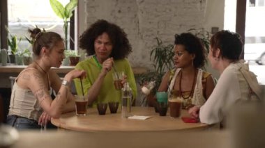 Farklı oryantasyonlardan 4k Arkadaşlar kokteyl içer ve barda masada konuşurlar. Genç lezbiyen kadınlar, eşcinsel bir adam gülücüklerle konuşuyor, bakıyor, alkol içiyor ve masada oturuyor. Olmayan Grup