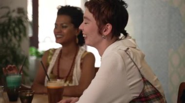 4K Lgbt kadınları, erkekler kafedeki masada eğlenir ve kokteyl içerler. Gülümseyen, gülen, içki içen ve kafeteryada masa başında oturan güzel homoseksüel insanların yakın çekimi. Grup