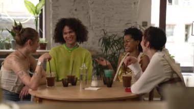 Farklı oryantasyonların 4k Dostları barda masada konuşur ve içerler. Güzel lezbiyen kadınlar, gülümseyen ve kutlayan bir adam, içecek içen ve iç kısımda masa başında oturan. Çoklu Etnik