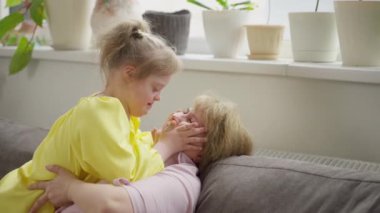 4K video. Down sendromlu bir kız sıcak bir odada kanepede otururken annesini kucaklıyor. Şu anda erken müdahale ve Down sendromlu çocuklar için özel eğitim planlarının altını çiziyoruz.