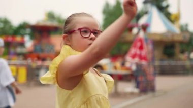 Lunaparkta, sarı elbiseli Down sendromlu genç kız fırıldak ile oynuyor. Yüzü merakla, sevinçle dolu. Sahne, özel ihtiyaçları olan bir çocuğa bakmanın mutluluğunu vurgular