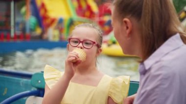 Lunaparkta, sarı elbiseli Down sendromlu bir kız annesinin izlediği dondurma külahının tadını çıkarıyor. Sahne, özel ihtiyaçları olan bir çocuğa bakmanın zevkini vurgular. Yüksek kalite 4k görüntü