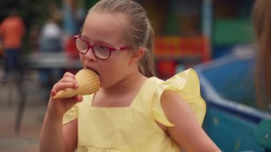 Renkli bir lunaparkta Down sendromlu genç bir kız annesi yanında otururken dondurma külahının tadını çıkarıyor. Sahne, çocuğu özel ihtiyaçlarla beslemenin mutluluğunu yansıtır. Yüksek kalite 4k