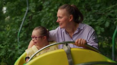 Lunaparkta, Down sendromlu anne ve küçük kızı eğlenceli bir gezinti yapıyorlar. Kızlar gülüyor ve anneler gülüyor. Özel ihtiyaçları olan bir çocuğa bakmanın mutluluğunu yansıtıyorlar. Yüksek kalite 4k