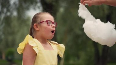 Sarı elbiseli Down sendromlu kız yaz aylarında annesinin yardımıyla mutlu bir şekilde pamuk şeker yiyor. Sahne, özel ihtiyaçları olan bir çocuğun ebeveynlik yolculuğunu ön plana çıkarıyor. Yüksek