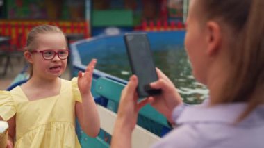 Down sendromlu kızı lunaparkta dondurmasıyla poz verirken anne telefonuyla fotoğraf çekiyor. Sahne, özel ihtiyaçları olan bir çocuk yetiştirmenin neşe ve özel anlarını yakalar. Yüksek