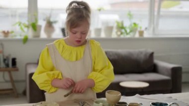 Down sendromlu 10 yaşında bir kız seramik atölyesinde çeşitli el yapımı çömlek parçalarıyla oynuyor. Farklı eserleri keşfeder, dahil etme ve çocuklar için fırsatlar sunar.