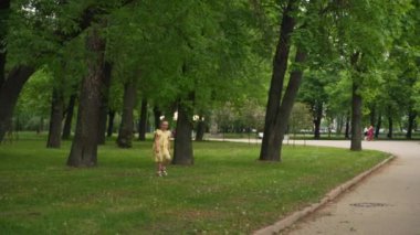 Down sendromlu sarı elbiseli genç bir kız ağaçlardan parktaki patikaya doğru koşuyor. Sahne, doğal çevrede hareketi ve özgürlüğü, konsepti yakalar. Yüksek kalite 4k görüntü