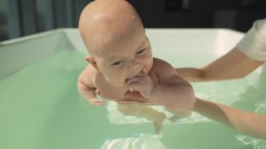 Modern apartmanda yüzme dersleri sırasında eğitmen bebeğe rehberlik eder. Bebek yüzmeye büyük ilgi gösteriyor, eğitmen destekleyici, güvenli bir ortam sağlıyor ve erken yüzme becerilerini ön plana çıkarıyor. Yüksek