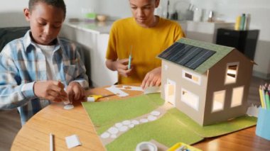 Güneş enerjisiyle çalışan mukavva ev modelinin yakın plan çekimlerinden masada kardeş el işi okul projesine geniş açılı görüntülere geçiş. Takım çalışması kavramı. Yüksek kalite 4k görüntü