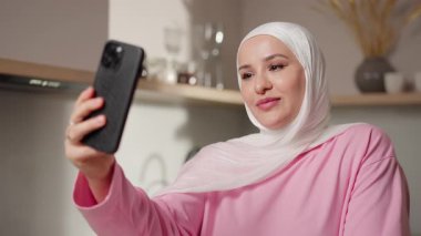 Video çağrısında, beyaz tesettürlü Müslüman kadın ekranla göz temasını sürdürürken nazikçe başını sallıyor. Onun ifadesi empati ve odaklanma gösteriyor. Anlamlı sanal etkileşim kavramı. Yüksek
