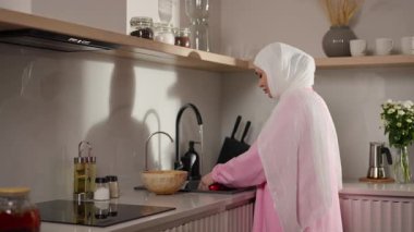 Hijyene odaklanmış, beyaz tesettürlü Müslüman kadın mutfak lavabosundaki meyveleri nazikçe yıkıyor. Onları hizmete hazırlamak için titizlikle hareket ediyor. Evde bakım ve sağlıklı alışkanlıklar kavramı. Yüksek