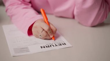 Beyaz masa üzerinde pembe tesettürlü Müslüman bir kadının dönüş formunu doldurması. Gerekli detayları tamamlamak için turuncu kalemle yazıyor. Çevrimiçi alışveriş ve geri dönüş kavramı. Yüksek
