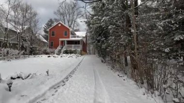Ocak ayındaki kar fırtınasından sonra kar yağan kırmızı banliyö evinin önünde yürüyorum.