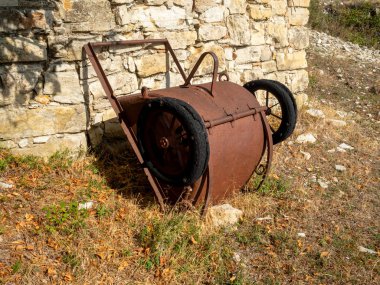 Fransa 'nın güney Alplerinde tepelerdeki eski taş barakanın yanında tekerlek üstünde paslı kova.