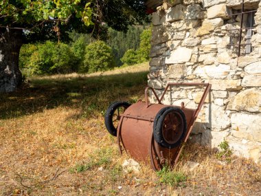 Fransa 'nın güney Alplerinde tepelerdeki eski taş barakanın yanında tekerlek üstünde paslı kova.