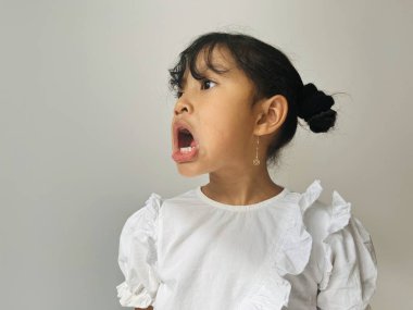 Beş yaşında, Asyalı, beyaz tişörtlü, öfkeli bir jest yapan küçük bir kız. Kaba çocuk konsepti