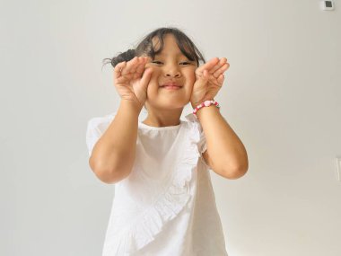 Beyaz gömlek giyen şirin Asyalı küçük kız kameraya şirin pozlarla bakıyor. Mutlu çocuk konsepti