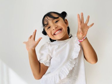 Beyaz gömlek giyen şirin Asyalı küçük kız kameraya şirin pozlarla bakıyor. Mutlu çocuk konsepti