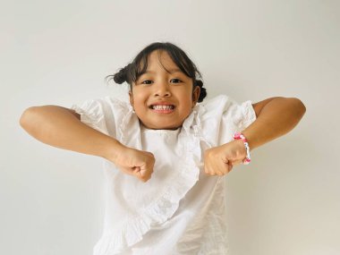 Komik bir hareket. Asyalı küçük kız iki elini kaldır ve yumruğunu sıkıp kameraya bak.