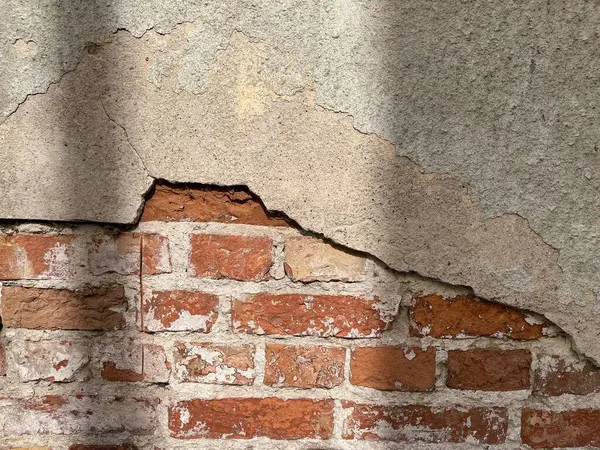 Yıpranmış, alçılı tuğla bir duvar. Tuğlalar zengin, kırmızımsı kahverengiye boyanmış ve harç rengi biraz solmuş. Alçı yontuluyor, altta yatan tuğlaları ortaya çıkarıyor..