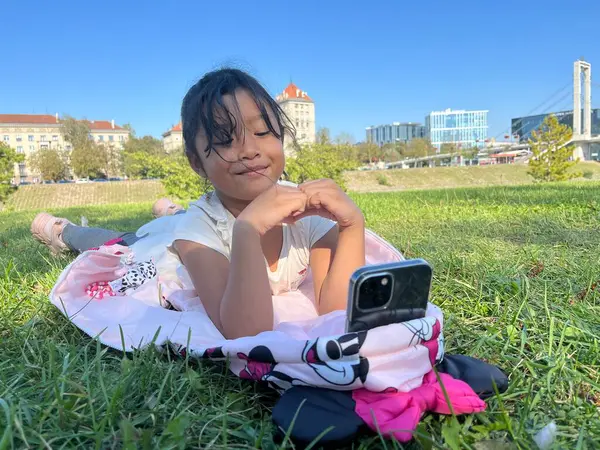 Mutlu Asyalı küçük kız dışarıda telefon kullanıyor. Aşk işareti el hareketleriyle video görüşmesi yapıyor.