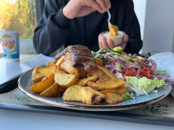 Tanınmayan bir adam, restoranda beyaz bir masada patates kızartması ve salatayla kebap yiyor.