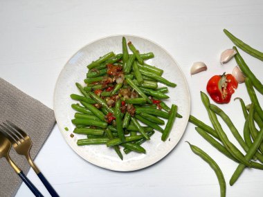 Sarımsaklı yeşil fasulye ve beyaz tabakta kırmızı biber. Asya usulü yemek. Üst görünüm