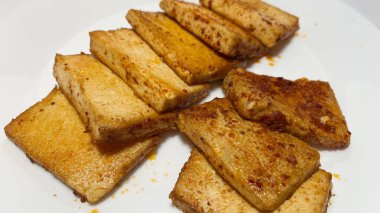 Beyaz tabakta Tayland baharatlı kızarmış tofu dilimleri.