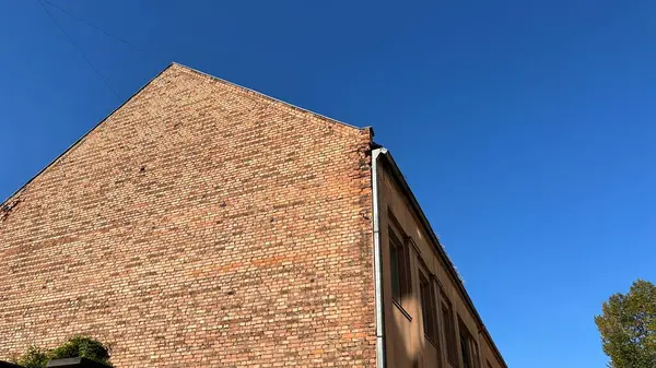 Ilık güneş ışığıyla yıkanmış yıpranmış tuğladan bir duvar, açık mavi gökyüzüne karşı. Duvar kâğıdı, tasarım unsuru ya da ticari amaçlar için mükemmel..
