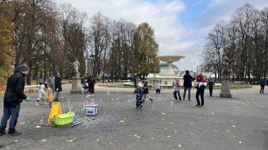 Warsaw, Poland. November 01, 2024. Park atmosphere in autumn with a man making soap bubbles and children enjoying the flying soap bubbles. clipart