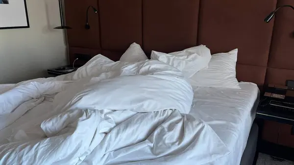 Beyaz çarşaflı, yastıklı, buruşuk ve dağınık bir yatağın yakın çekimi.
