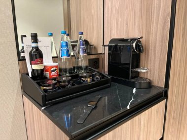 Varşova, Polonya. Kasım 02, 2024. Çeşitli imkanları olan bir otel odası mini barı. Sade bir kahve makinesi, bir şişe su, şarap, kahve kapsülleri ve diğer atıştırmalıklar.