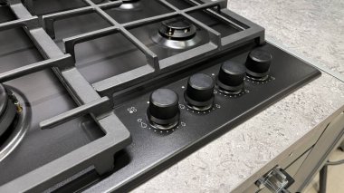 Çoklu yakıcı ve kontrol düğmeleri olan modern bir gaz ocağına yakın çekim, desenli bir tezgaha ayarlı.