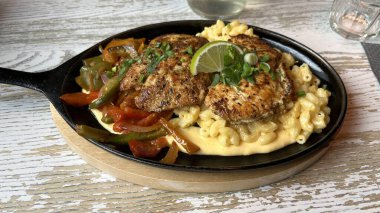 Baharatlı tavuk, kremalı makarna, peynir ve sotelenmiş sebzelerle dolu dökme demir tavanın yakın çekimi. Hizmet etmeye hazırım. Yemek blogları ya da yemek ile ilgili yayınlar için mükemmel.