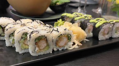 İki çeşit suşi rulosunun yer aldığı bir tabağın yakından çekimi. Tabak koyu dikdörtgen bir tabakta duruyor. Japon mutfağı, deniz ürünleri ve sağlıklı beslenme kavramı..