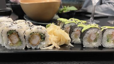 İki çeşit suşi rulosunun yer aldığı bir tabağın yakından çekimi. Tabak koyu dikdörtgen bir tabakta duruyor. Japon mutfağı, deniz ürünleri ve sağlıklı beslenme kavramı..