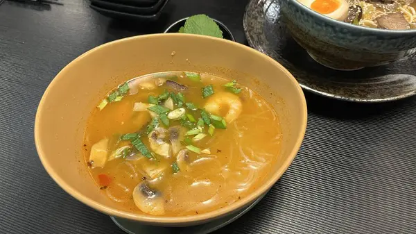 Bir kase Tom Yum çorbası, geleneksel Tayland sıcak ve ekşi çorbası. Koyu dokulu bir masada turuncu bir kasede servis edilmiş. Otantik Tayland mutfağı, sağlıklı yemek ve lezzetli yemek konsepti.
