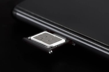 Koyu arkaplanda bir akıllı telefonun SIM kart tepsisine eklenen SIM kart