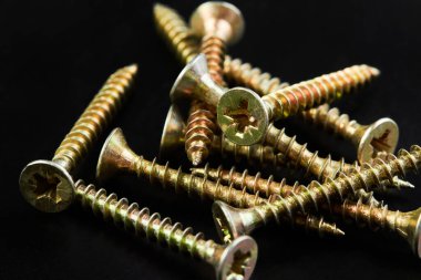 Vidalar yığını ya da siyah arka planda sarı kaplamalı kendi kendine tıkırdayan vidalar.