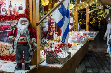 Noel Baba heykelciğinin, Fin bayrağının ve rahat bir gece ortamında renkli tatil süslemelerinin yer aldığı Noel alışverişi tezgahı.