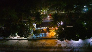 Tropikal ağaçlarla çevrili ve sıcak ışıklarla aydınlatılmış sakin bir sahil kenarı inzivasının hava gece görüşü. Yüksek kalite fotoğraf